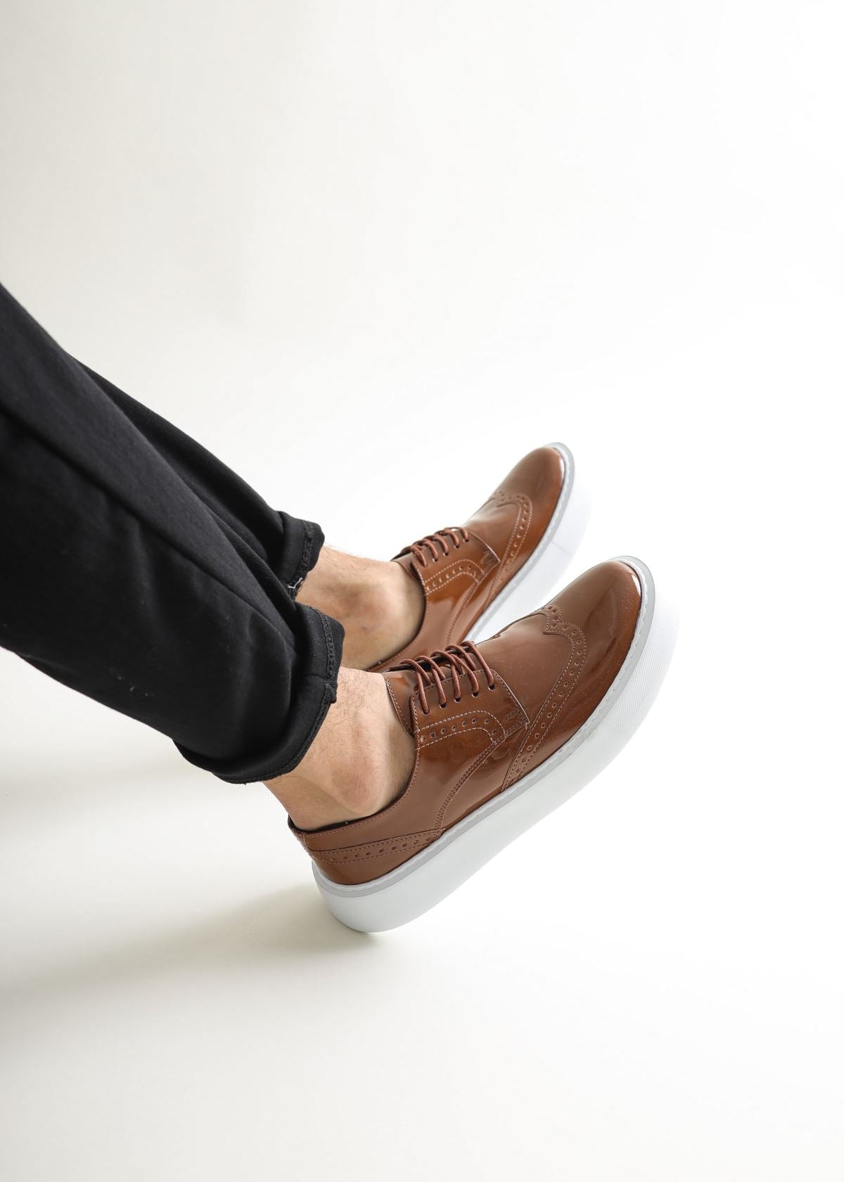Brown shoes with white soles worn by a person on a light gray background
